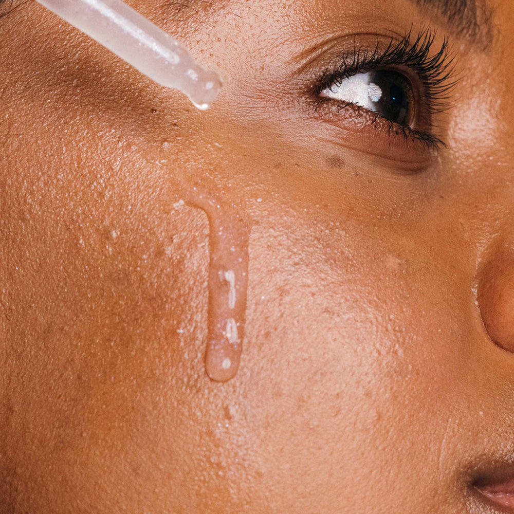 Close-up of a woman applying a dropper of liquid to her skin.