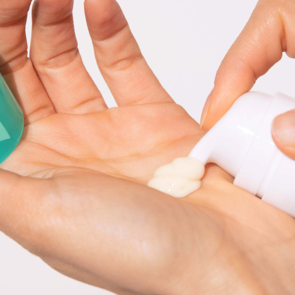 Hand applying blackhead clearing fizz mask from a tube onto the palm against a white background
