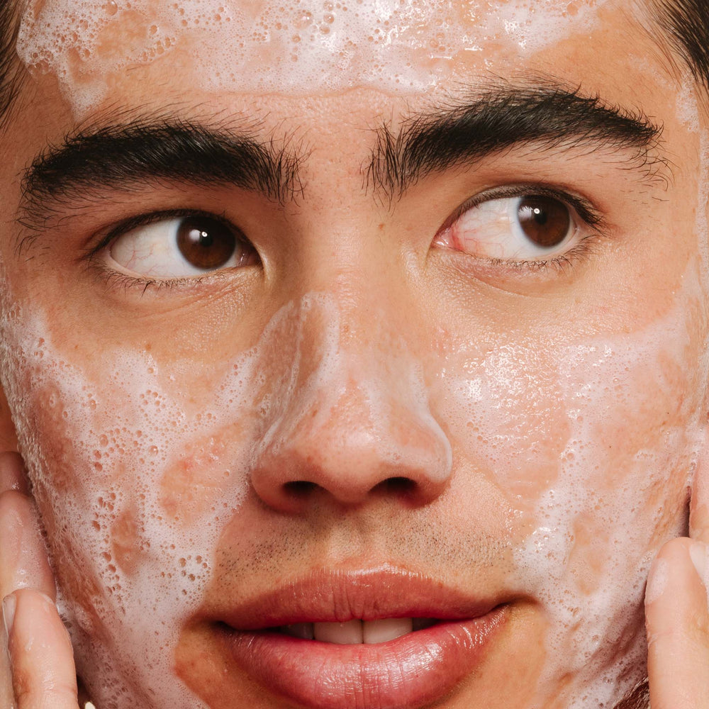 Close-up of a person applying a breakout clearing cleanser with soapy foam on their face.